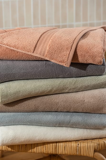 A stack of folded Capyhome towels in earthy tones on a rattan bench