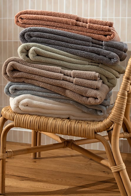 Folded Capyhome towels in soft earthy shades resting on a rattan chair