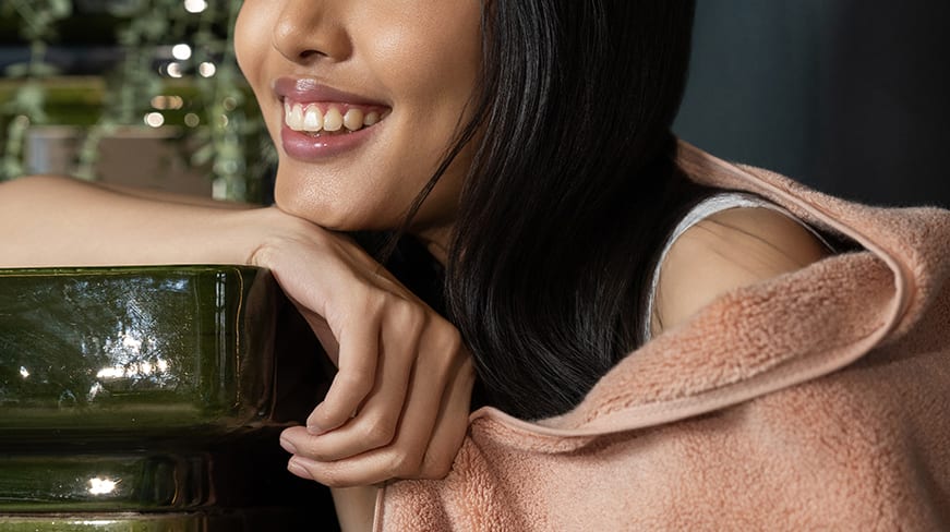 A woman in a blush Capyhome robe smiling in a warm, plant-filled room