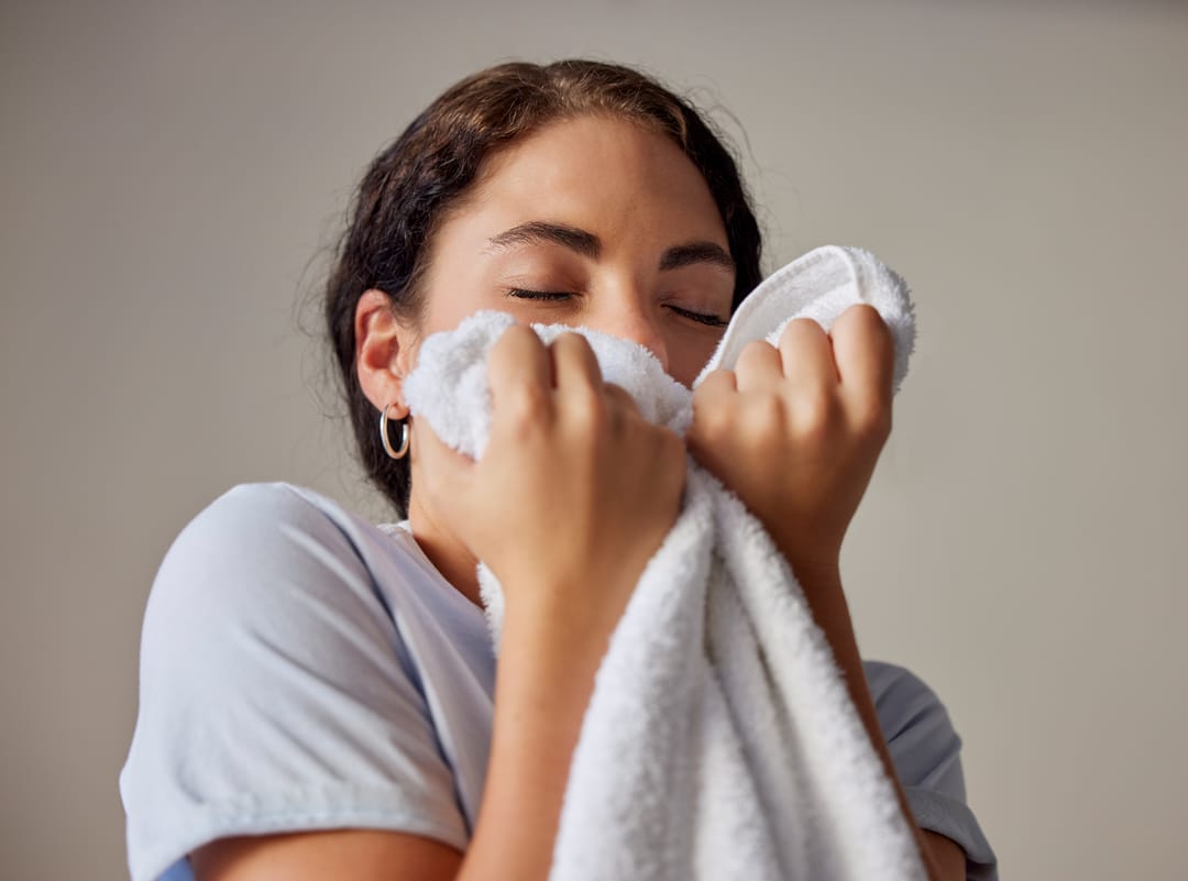 woman pressing a freshly washed white cotton towel to her face with her eyes closed