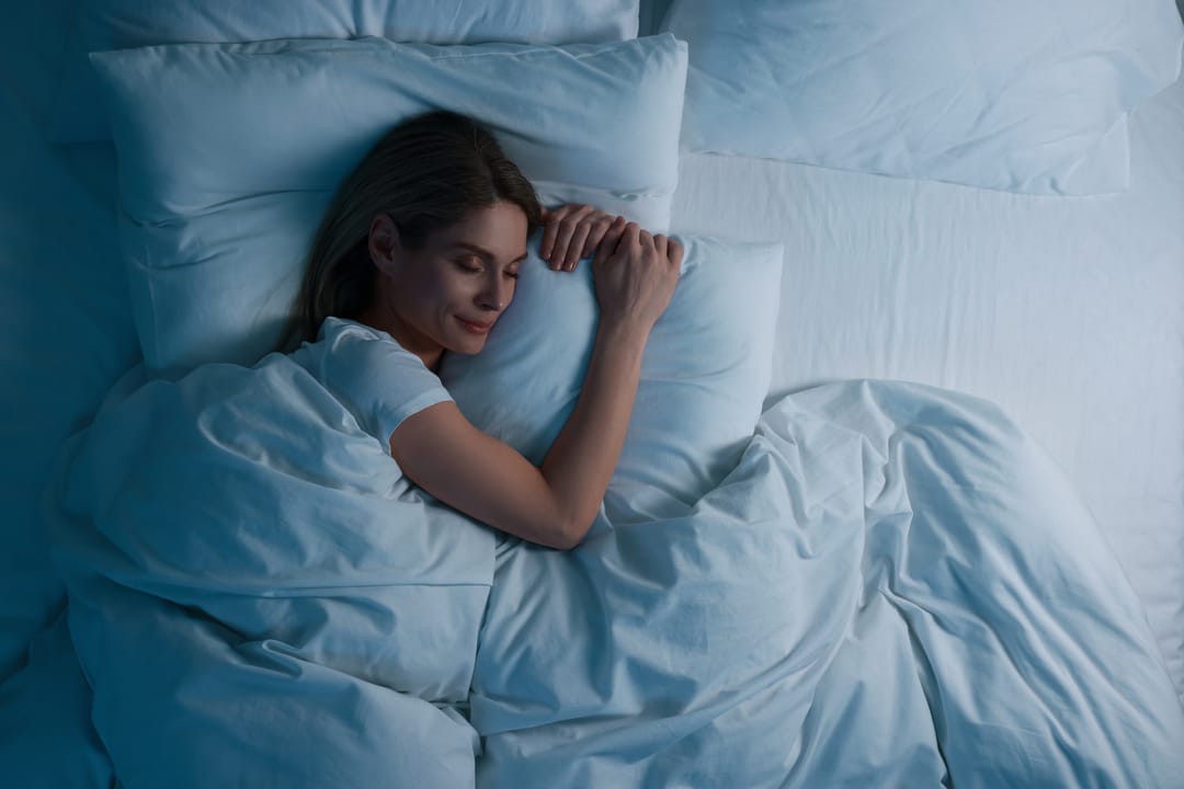 woman sleeping comfortably under soft cotton bedding at night, seen from above