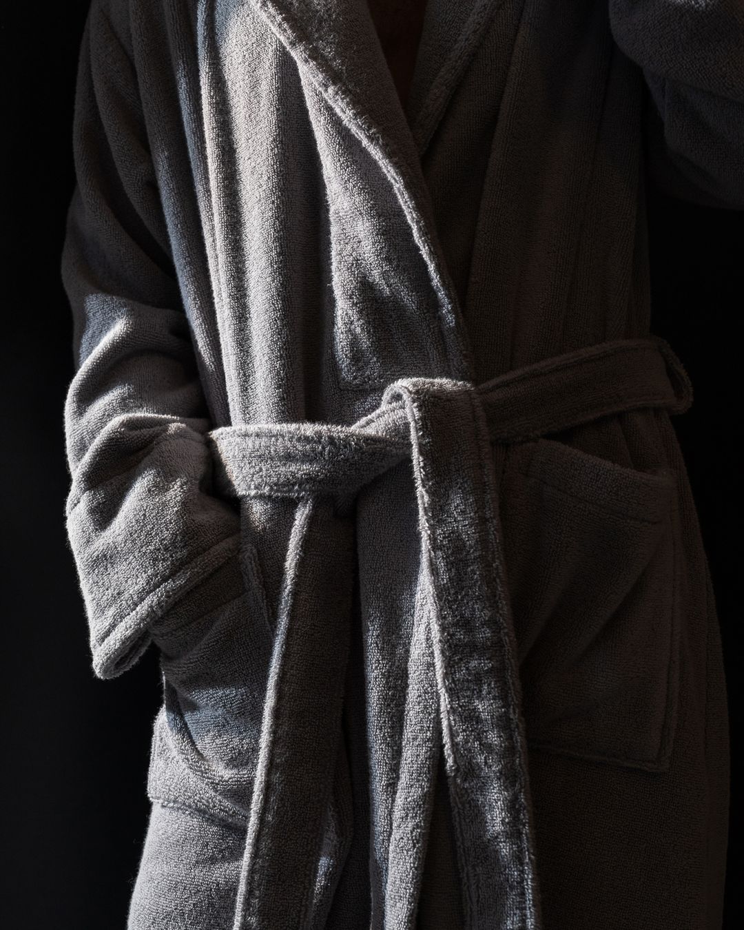 close-up of a man wearing a thick grey plush robe tied at the waist, showing its dense terry texture