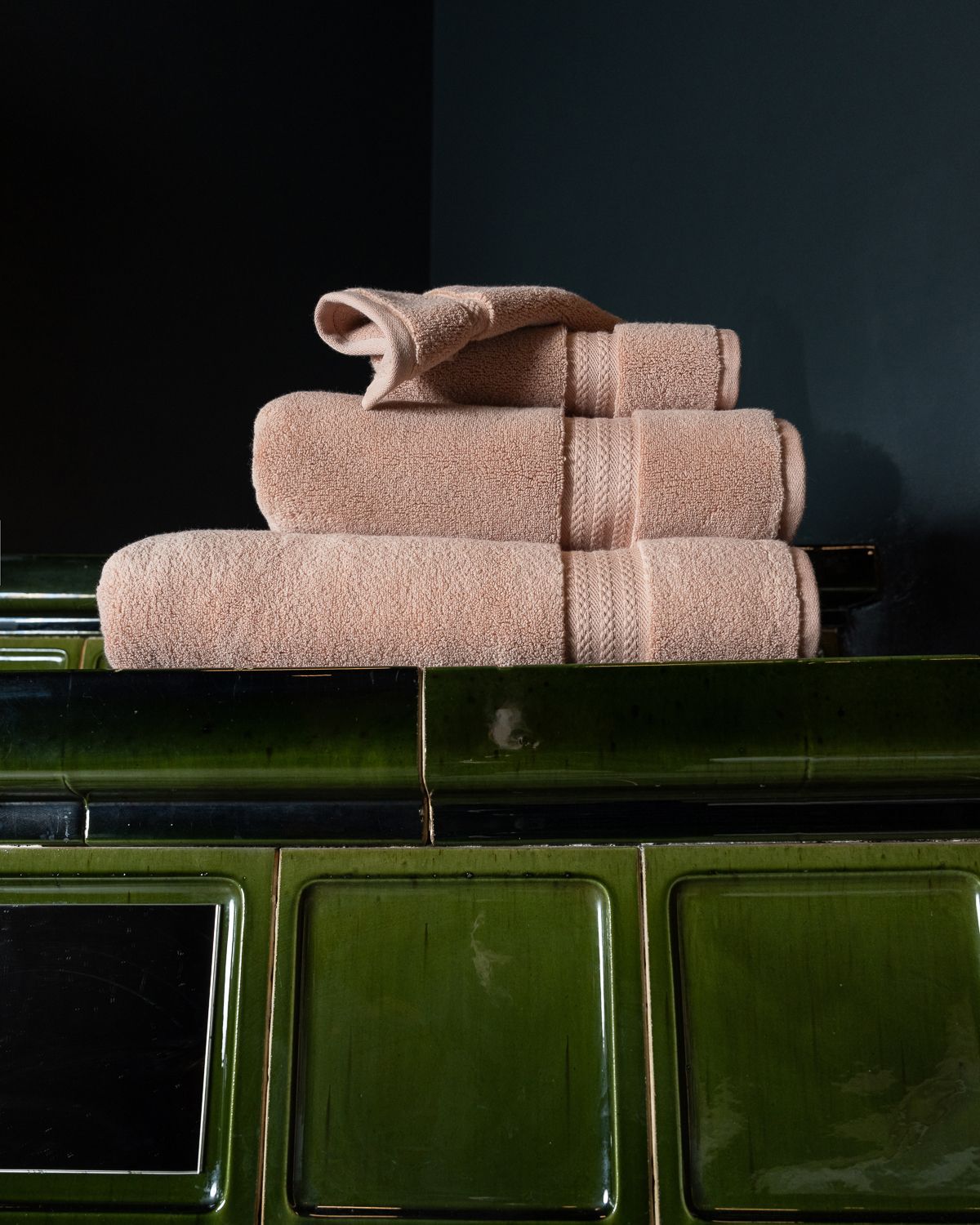 Folded capyhome Turkish cotton towels stacked on a green tiled stove