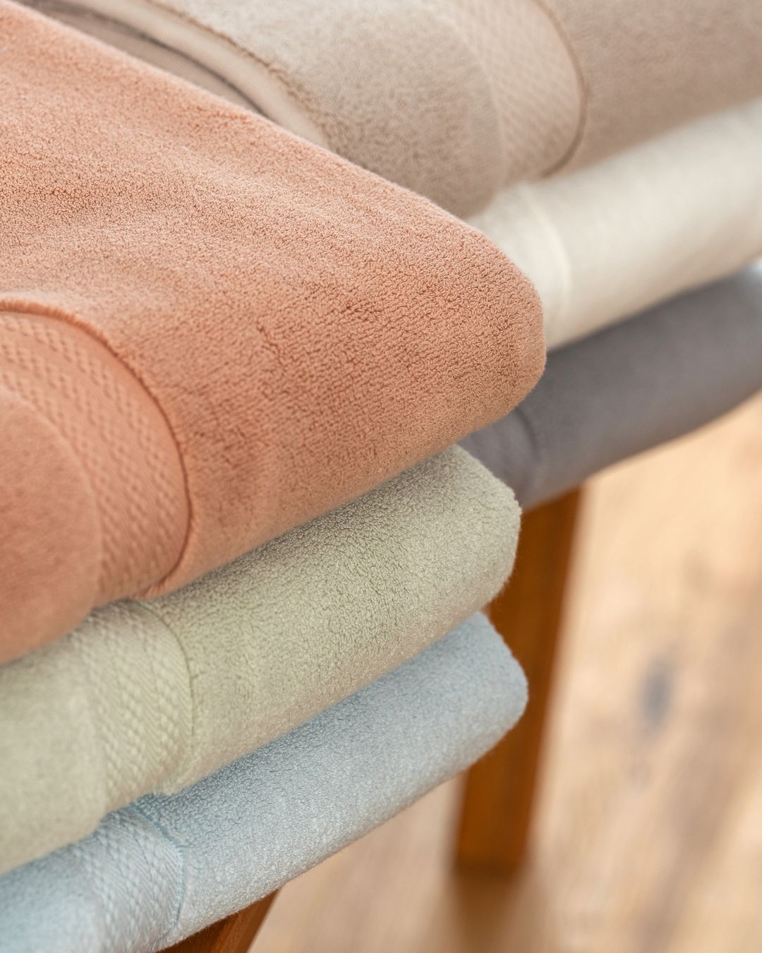 close-up of folded plush terry towels in clay, sage, and blue showing the soft looped weave