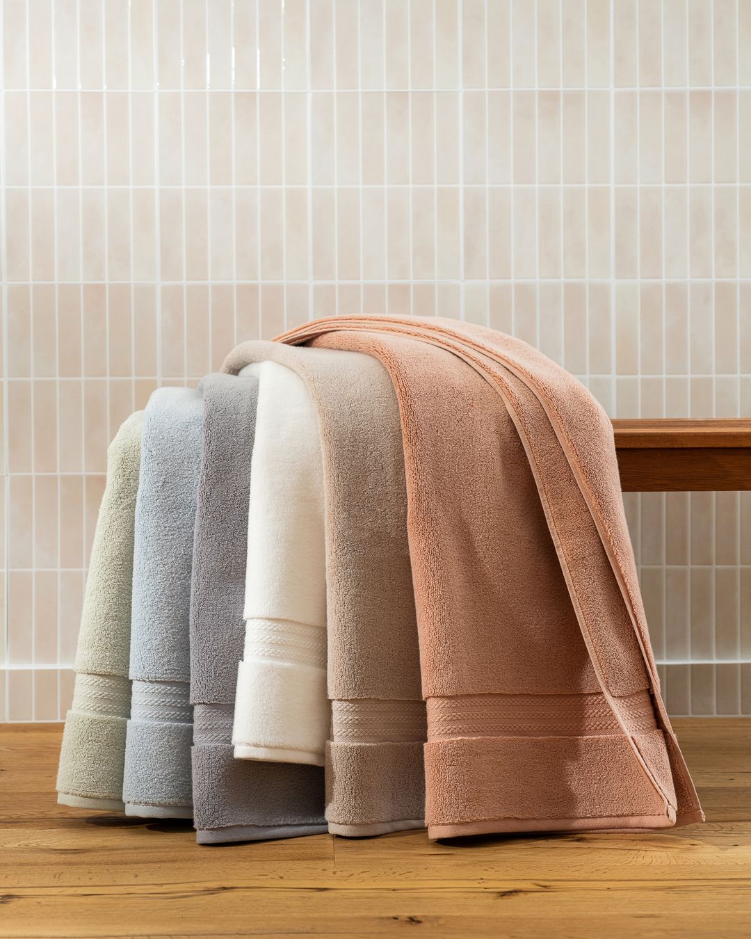row of plush Turkish cotton terry bath towels in soft colors draped over a wooden bench