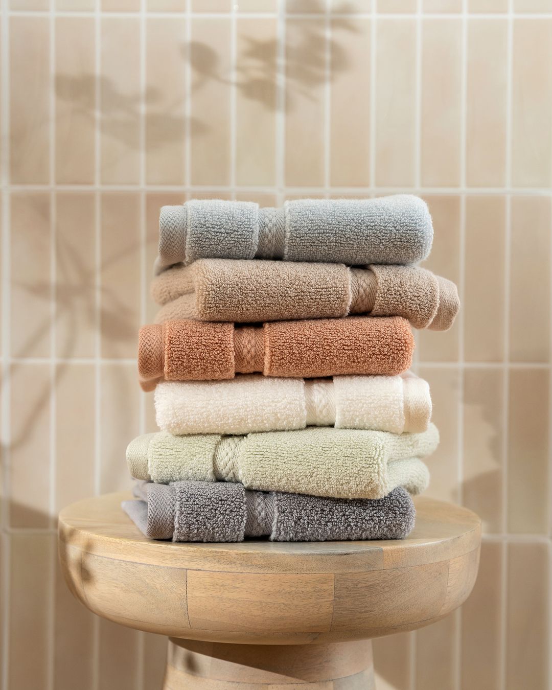 stack of folded Turkish cotton terry towels in gray, tan, terracotta, cream, and sage on a wooden stool