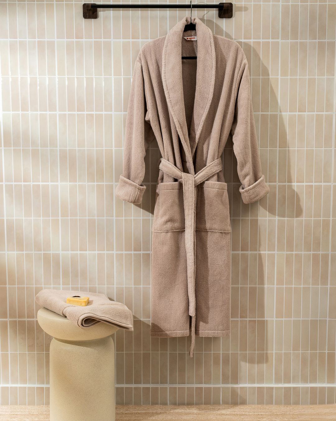beige cotton bathrobe hanging in a guest bathroom beside a stool with soap