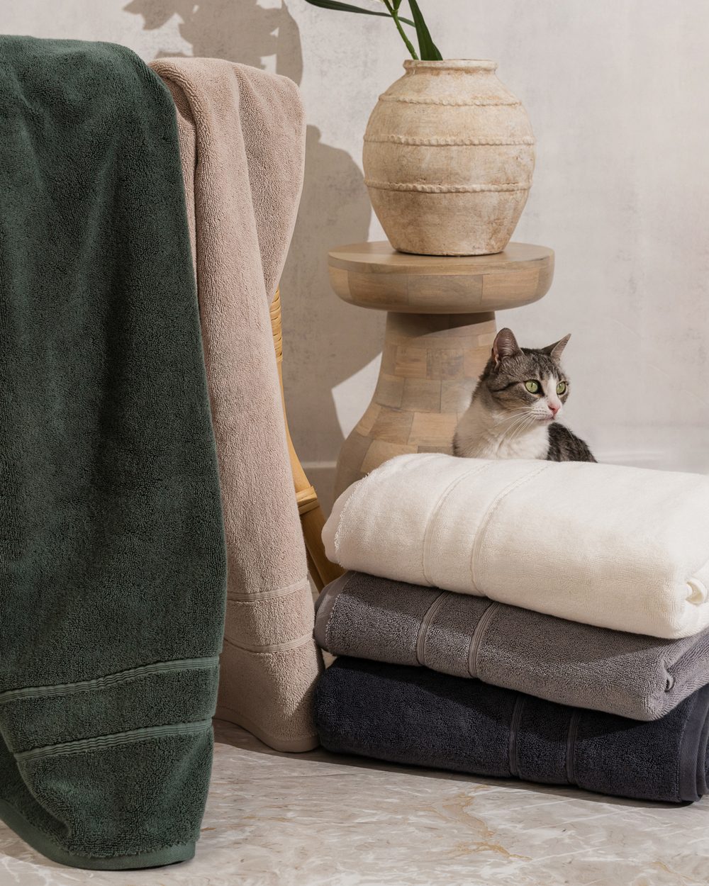 capyhome Turkish cotton towels in green, tan, cream and grey draped and stacked beside a curious cat