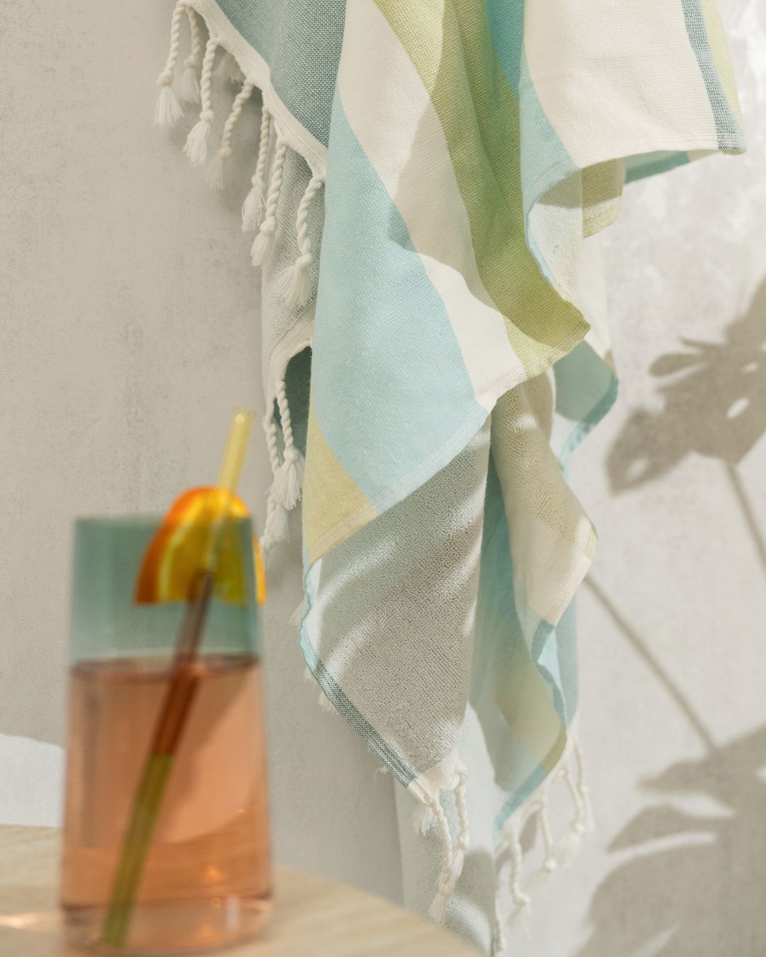 striped Turkish cotton peshtemal towel with hand-knotted fringe hanging on a wall beside a cold drink
