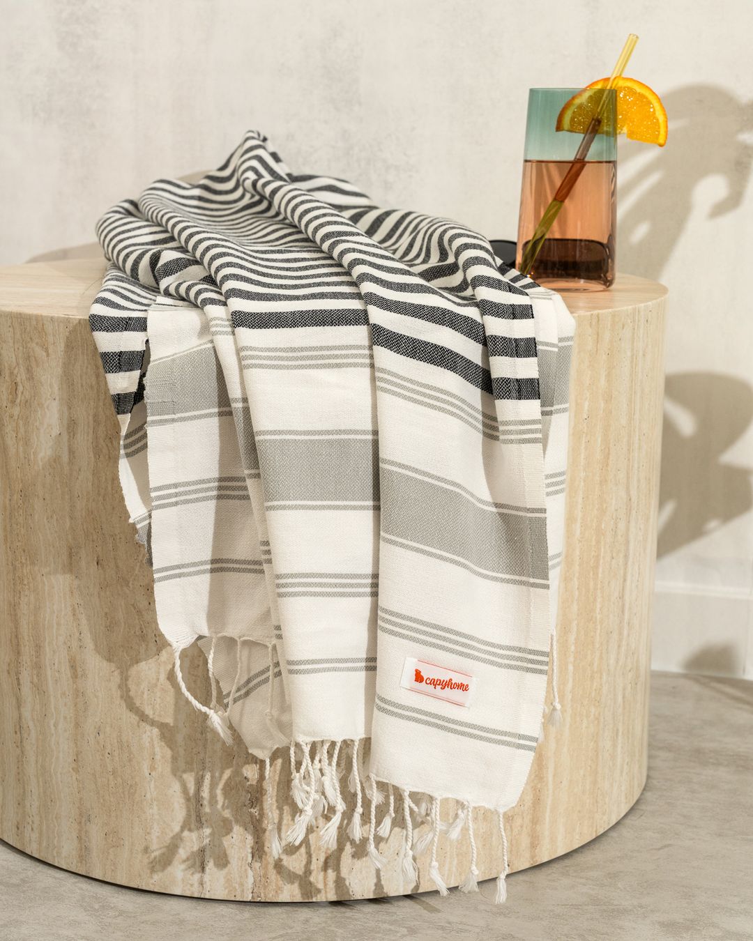 gray and white striped Turkish cotton beach towel with knotted fringe draped over a stone side table