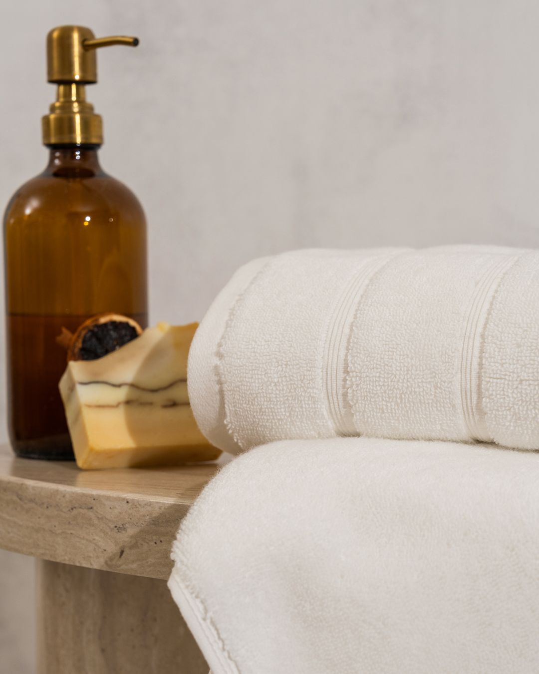 cream capyhome bath towel on a bench beside an amber soap dispenser