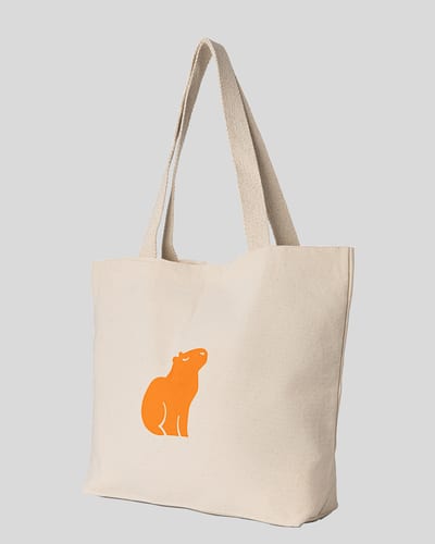 Natural canvas tote bag with an orange capybara print, angled view