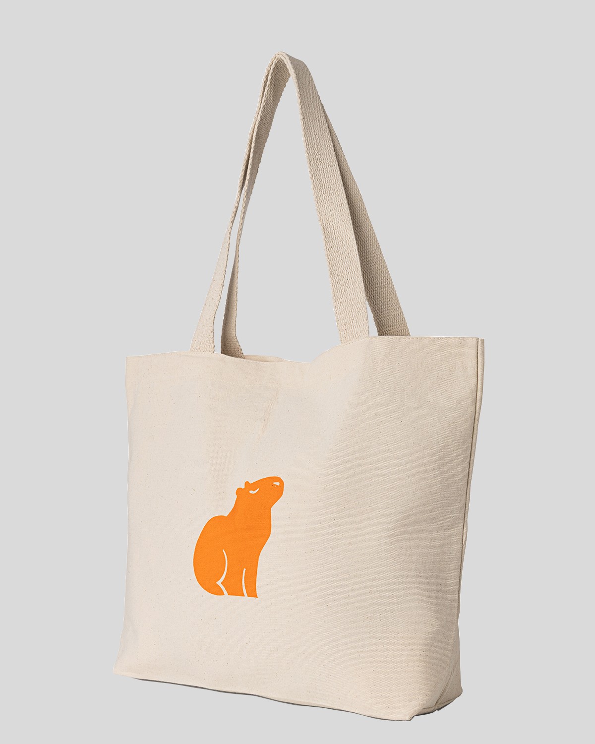 Natural canvas tote bag with an orange capybara print, angled view