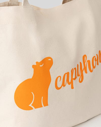 Close-up of a natural canvas tote bag with an orange capybara logo and capyhome script