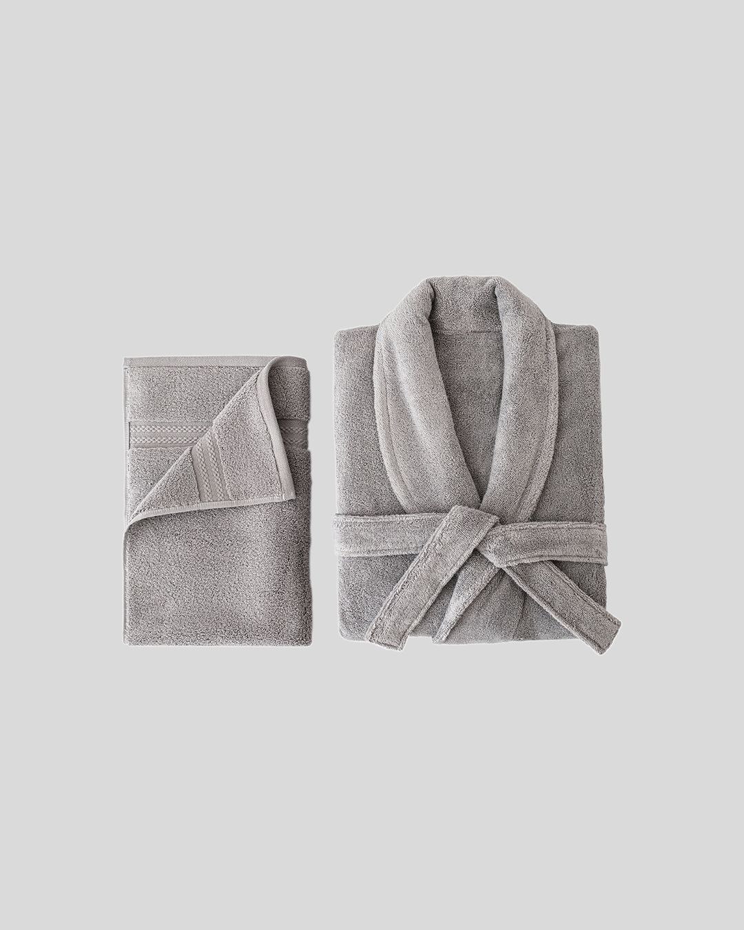 folded grey plush capyhome robe with a matching towel on a plain studio background