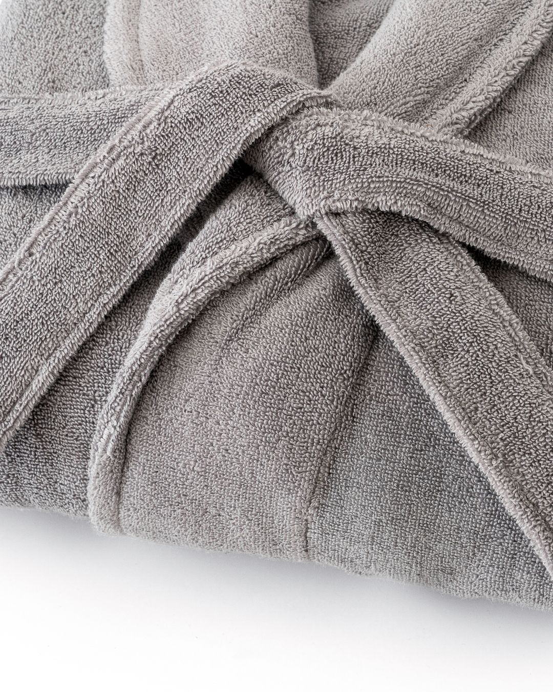 close-up of a folded grey terry cotton bathrobe with its belt tied, showing the looped pile on both sides of the fabric